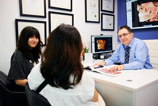 Orthodontist consulting with a child and her mother in the clinic